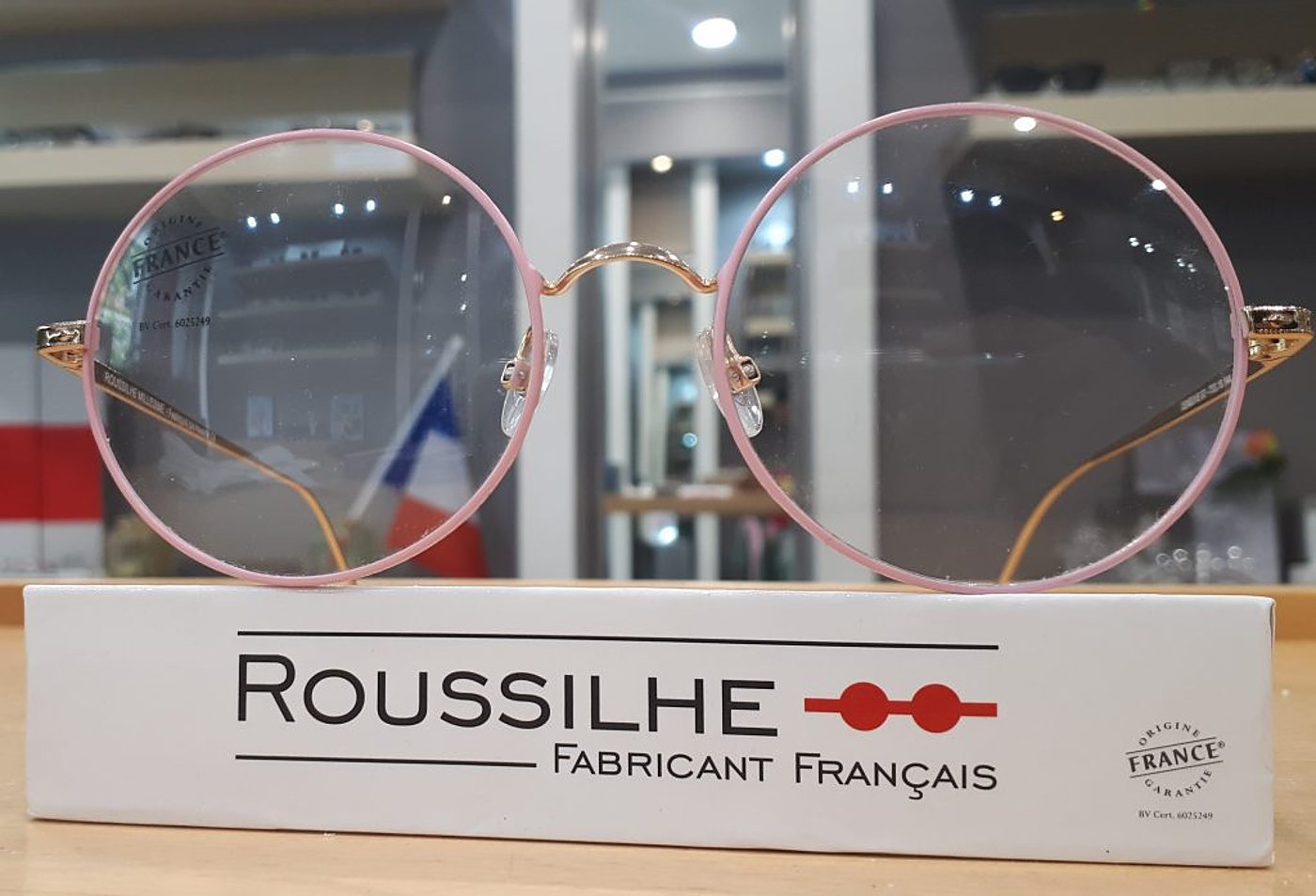 Lunettes rondes roses et dorées posées sur un boîtier Roussilhe