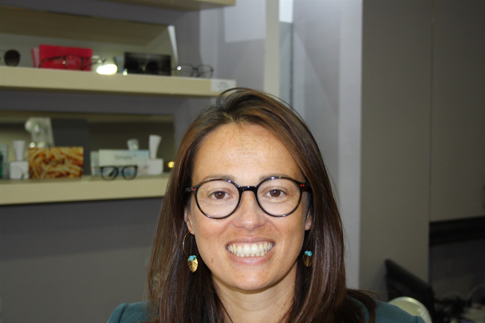 Portrait souriant d’une opticienne devant des étagères de lunettes